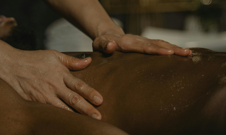 Mãos de mulher sobre o peito de homem moreno nu a ensinar como é feita a massagem nuru.